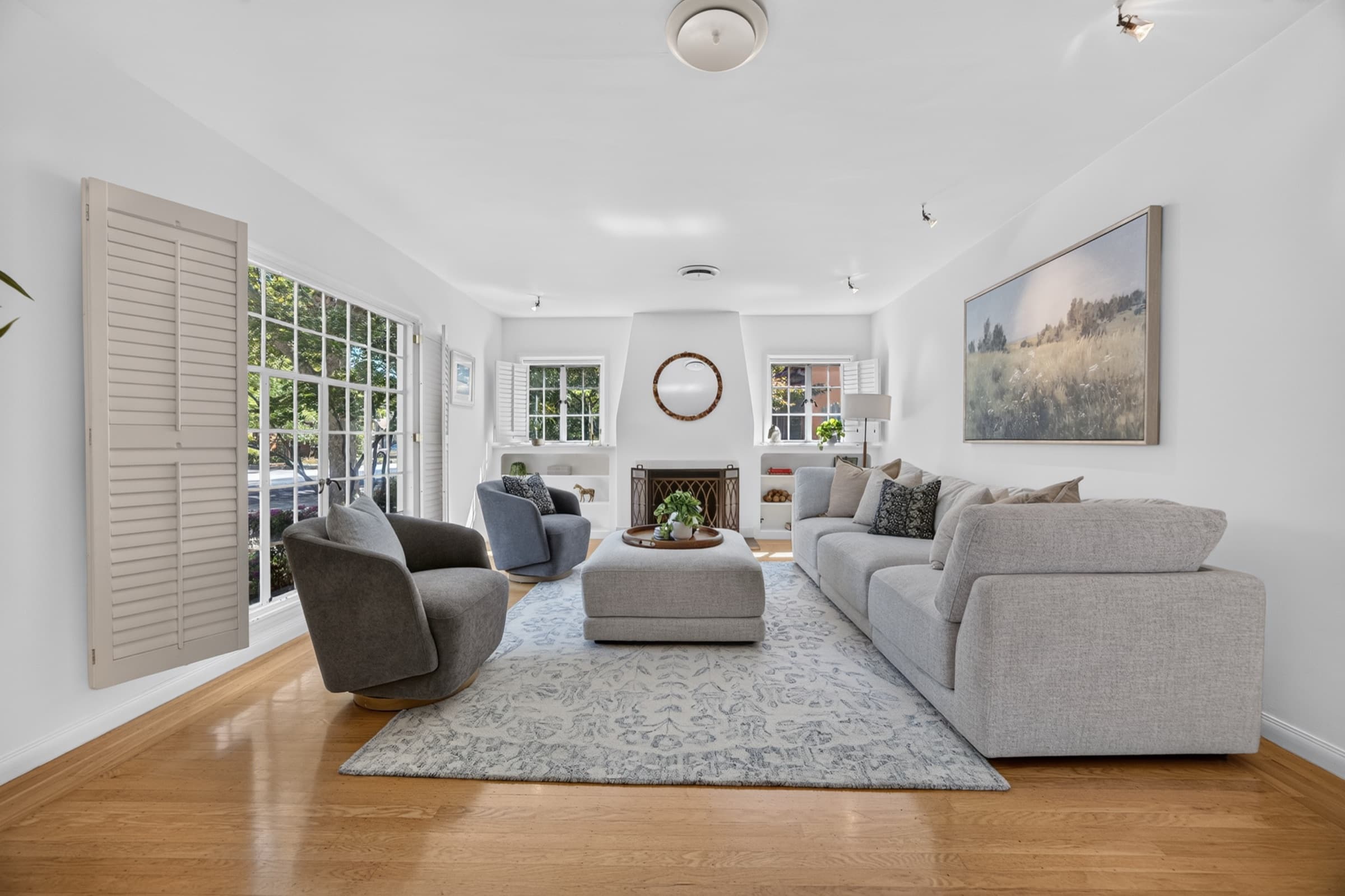A staged living room with a light gray sectional, two swivel chairs and a patterned rug